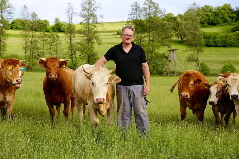 Bauer, der auf einer Wiese steht und liebevoll eine Kuh streichelt