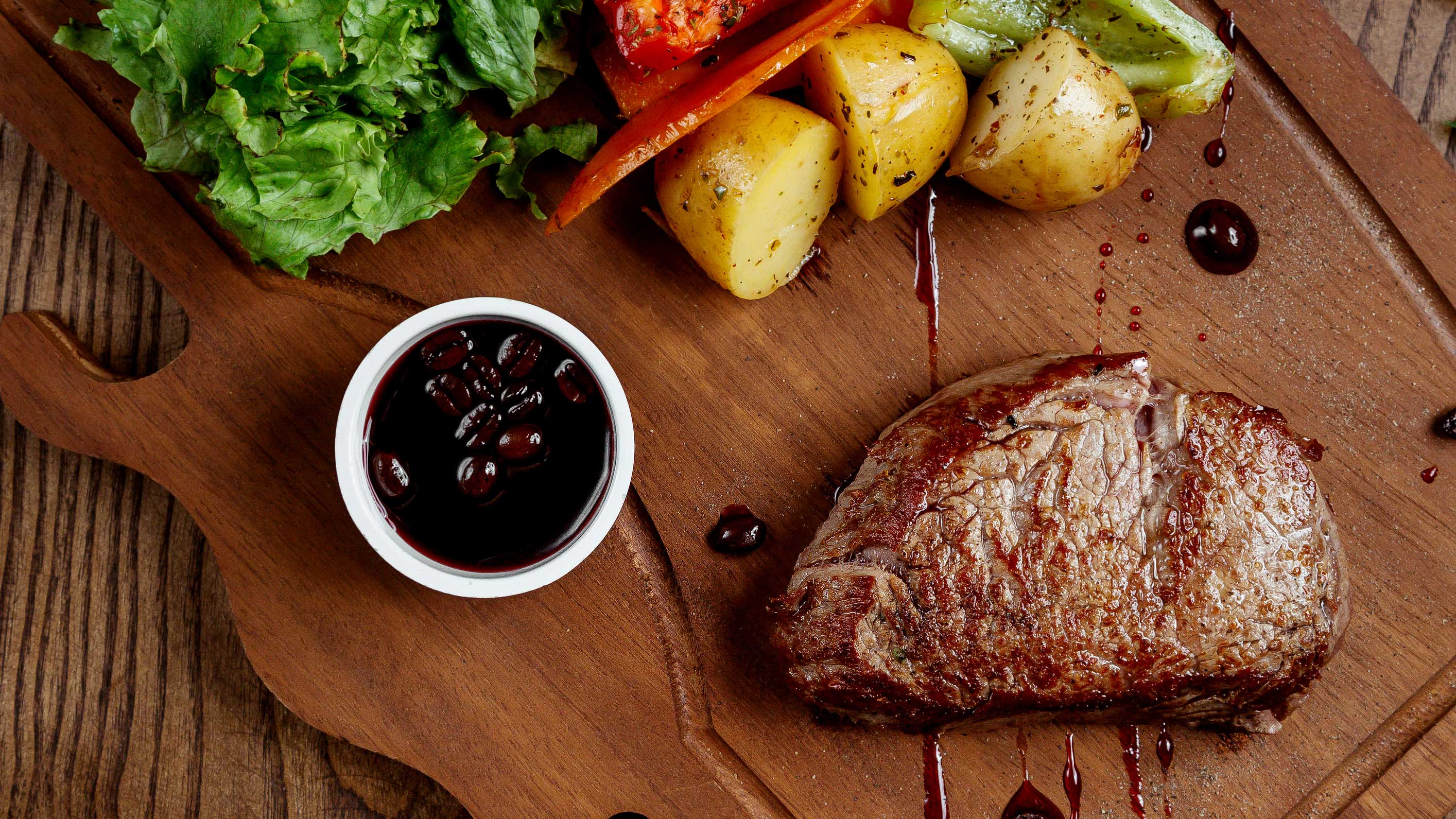 Gebratenes Wagyu Steak auf einem Holzbrett mit Kartoffeln, Salat und einer Schale Sauce